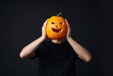 Cadılar Bayramı kutlaması. Siyah arka planda oyulmuş ürkütücü yüzü olan bir adam balkabağı tutuyor.