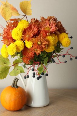 Sonbahar atmosferi. Güzel çiçekli vazo, böğürtlen ve balkabağı ahşap masada, yakın plan.
