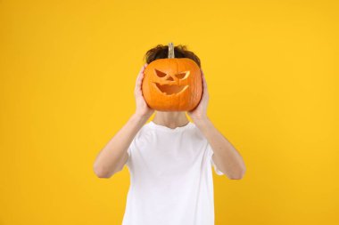 Cadılar Bayramı kutlaması. Çocuk, turuncu arka planda oyulmuş ürkütücü yüzlü balkabağı tutuyor.