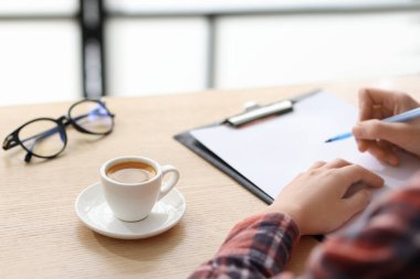 Kahve molası. Bir fincan aromatik içecek ve kapalı alanda ahşap masada çalışan bir kadın. Metin için boşluk