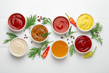 Tabaklardaki farklı soslar ve beyaz ahşap masa üzerindeki malzemeler.