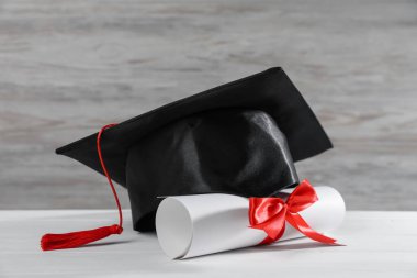 Mezuniyet şapkası ve diploması beyaz tahta masada, yakın plan.