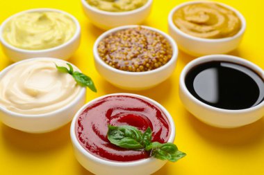 Sarı arka planda farklı soslar ve otlar, yakın plan.