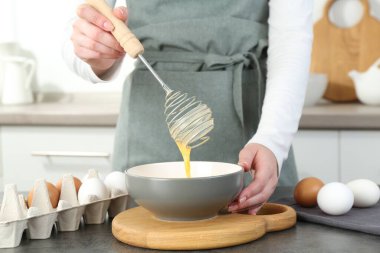 Mutfaktaki gri masada çırpılmış yumurta çırpan kadın, yakın plan.