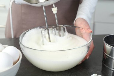 Mutfaktaki gri masada yumurta beyazını mikserle döven kadın, yakın plan.