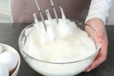 Mutfaktaki gri masada yumurta beyazını mikserle döven kadın, yakın plan.