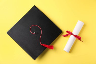 Sarı arka planda diploma ve mezuniyet şapkası.