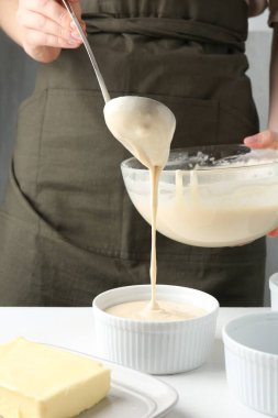 Kadın hamur hamurunu (sıvı hamur) içerideki masada yemek tabaklarına döküyor, yakın plan.