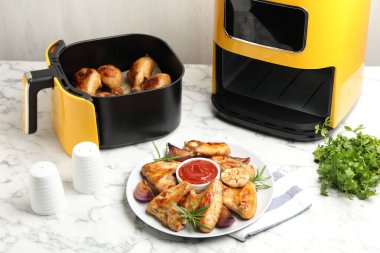 Lezzetli ızgara tavuk kanatları, sos ve baharatlar. Beyaz mermer masada pişirilmiş bagetlerle birlikte.