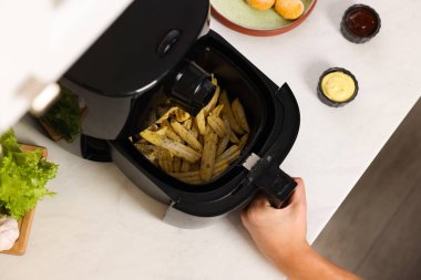 Beyaz mermer tezgahta patates kızartması pişiren bir adam var.