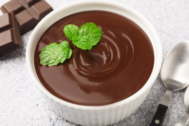 Erimiş çikolata, kasede nane şekeri, parçalar ve kaşık açık gri masada, yakın plan.