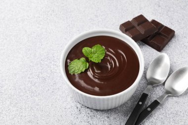 Erimiş çikolatayı kasede naneli, parçaları ve kaşıkları açık gri masada, yakın plan. Metin için boşluk