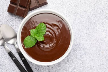 Erimiş çikolata kasede nane, parçalar ve kaşıklar açık gri masada, düz yatıyordu.