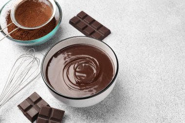 Erimiş çikolata kasede, parçalarda, kakao tozunda ve açık gri masada çırpılmış, yakın plan. Metin için boşluk