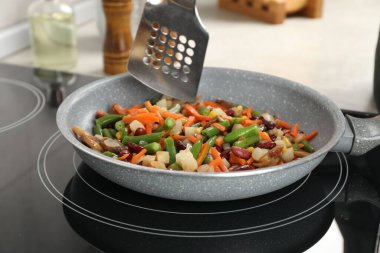 Kızartma tavasında sotatula ile taze sebzelerin karıştırıcı karışımı, yakın plan.