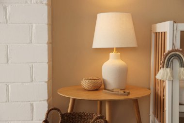 Beşik, masa, lamba ve dekorasyon. Bej duvarın yanında, mesaj için yer var. Şık bir bebek odası.