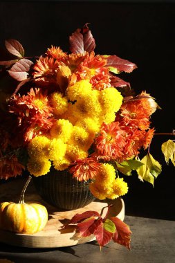 Sonbahar atmosferi. Üzerinde güzel çiçekler, yapraklar ve balkabağı olan vazo, siyah arka planda, yakın plan.