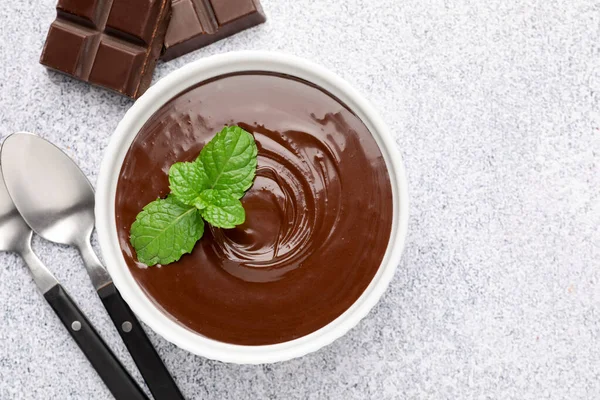 Erimiş çikolata kasede nane, parçalar ve kaşıklar açık gri masada, düz yatıyordu.