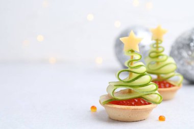 Kırmızı havyar, salatalık, peynir ve beyaz masa üzerindeki şenlikli dekordan yapılmış Noel ağacı şekilli turtalar.