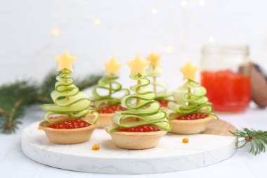 Kırmızı havyar, salatalık, peynir ve beyaz masa üzerindeki şenlikli dekordan yapılmış Noel ağacı şekilli turtalar.