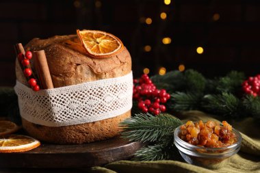 Noel yemeği. Lezzetli Panettone pastası, malzemeler ve arka planda arka planda bulanık ışıklı şenlikli dekor, yakın plan. Bokeh etkisi