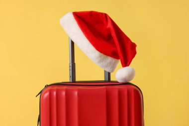 Sarı arka planda Noel Baba şapkası olan şık bir bavul, yakın plan. Noel tatili