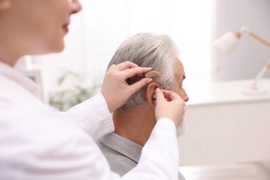 Doktor hastanede yaşlı adamın kulağına işitme cihazı takıyor.