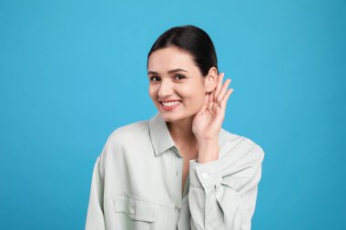 Açık mavi arka planda el ele hareketler gösteren genç bir kadın.