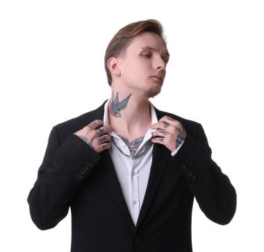 Piercingli, dövmeli ve beyaz arka planda poz veren şık elbiseli genç bir adam.