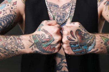 Dövmeli ve şık elbiseli genç adam koyu gri arka planda poz veriyor, yakın plan.