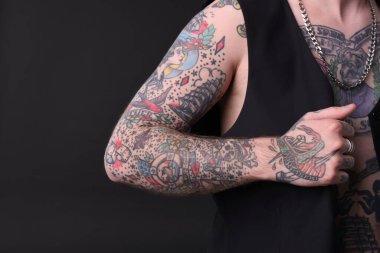 Dövmeleri ve şık elbiseleri olan, koyu gri arka planda poz veren genç bir adam, yakın plan. Metin için boşluk