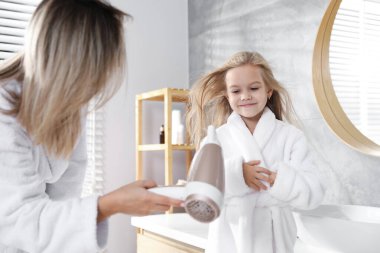 Bir kadın banyoda kızının saçını kurutuyor.