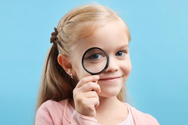 Açık mavi arka planda büyüteç takan küçük bir kız.
