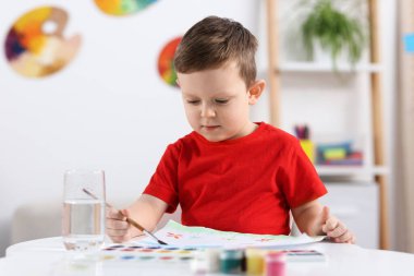 Beyaz masa içinde fırçayla çizim yapan sevimli küçük çocuk.