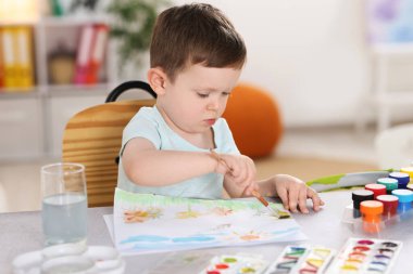 İçerideki gri masada fırça çizen sevimli küçük çocuk.