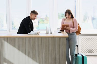 İçerideki resepsiyonda misafir ile çalışan resepsiyonist.