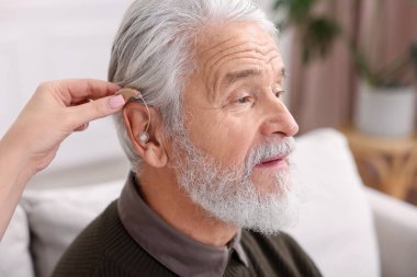 Bakıcı, kıdemli adamın evde işitme cihazı takmasına yardım ediyor.