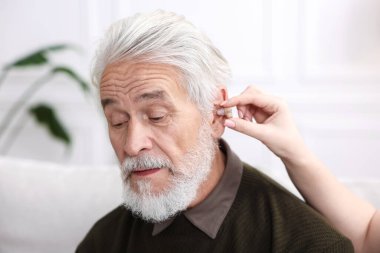 Bakıcı, kıdemli adamın evde işitme cihazı takmasına yardım ediyor.