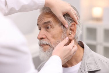 Doktor hastanede yaşlı adamın kulağına işitme cihazı takıyor.