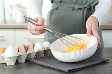 Mutfaktaki gri masada çırpılmış yumurta çırpan kadın, yakın plan.