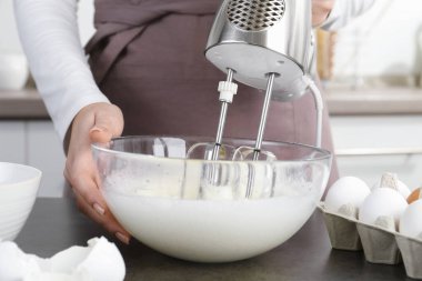 Mutfaktaki gri masada yumurta beyazını mikserle döven kadın, yakın plan.