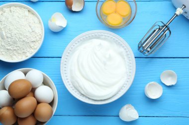 Kasede çırpılmış yumurta beyazı, mikser ve ürünler mavi ahşap masada, düz yerde.