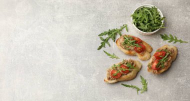 Lezzetli bruschettalar, ton balığı, domates ve roka, gri masada, düz. Metin için boşluk
