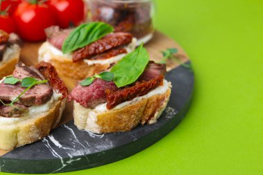 Biftek, krem peynir, fesleğen, güneşte kurutulmuş domatesler ve yeşil arka planda taze sebzeler, yakın plan. Metin için boşluk