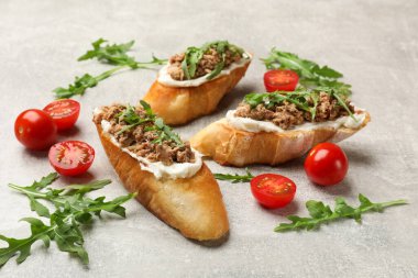 Ton balıklı lezzetli bruschettalar, domatesler ve roka gri masada, yakın plan.