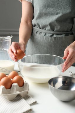 Hamur yapmak (sıvı hamur). Beyaz masadaki kaseye yumurta ekleyen kadın, yakın plan.