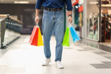 Farklı alışveriş çantaları olan bir adam alışveriş merkezinde yürüyor.