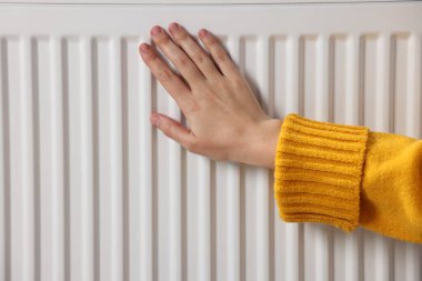 Kadın elini radyatörün yanında ısıtıyor, yakın plan.