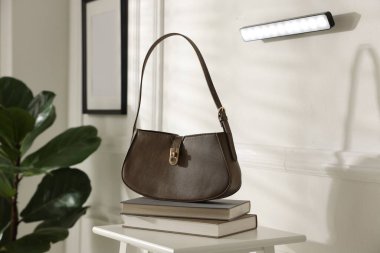 Beyaz duvarda şık bir LED lamba, kitaplarla dolu tabure ve kapalı bir çanta.