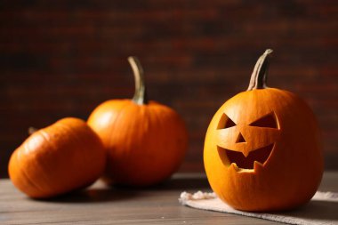 Cadılar Bayramı kutlaması. Tuğla duvara karşı ahşap masada oyulmuş balkabakları, yakın plan.